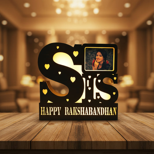 Decorative light with 'SIS' and 'Happy Rakshabandhan' text, featuring a small inset photo of a woman.