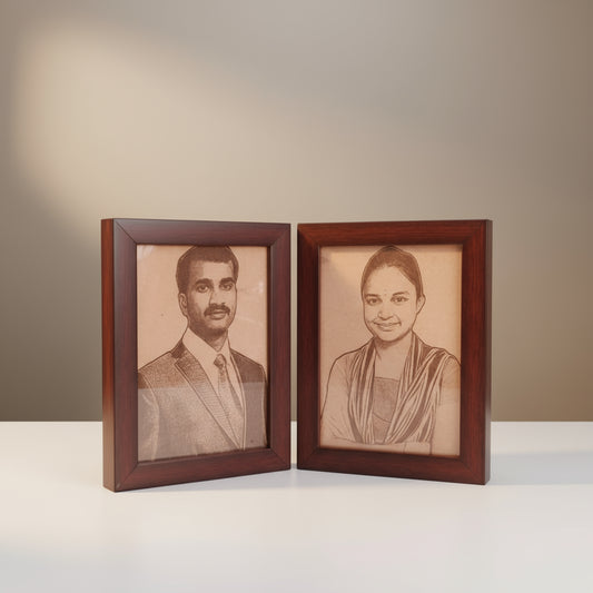 Two framed portraits of a man and a woman on a wooden surface with a green leafy background.